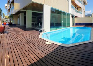 Ein Poolbereich mit Holzterrasse, einem Wintergartenbalkon und Kübelpflanzen.