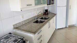 A kitchen with white cabinets, a granite countertop, a double sink, a gas stove, a coffee maker, and a refrigerator. - Ap Premium na Lagoa (Florianópolis)
