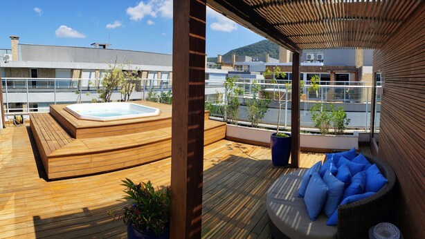 Een terras op het dak met een jacuzzi, houten zitplaatsen en plantenbakken.