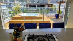 Een moderne keuken met een gasfornuis, een eethoek met blauwe stoelen en uitzicht op een dakzwembad.