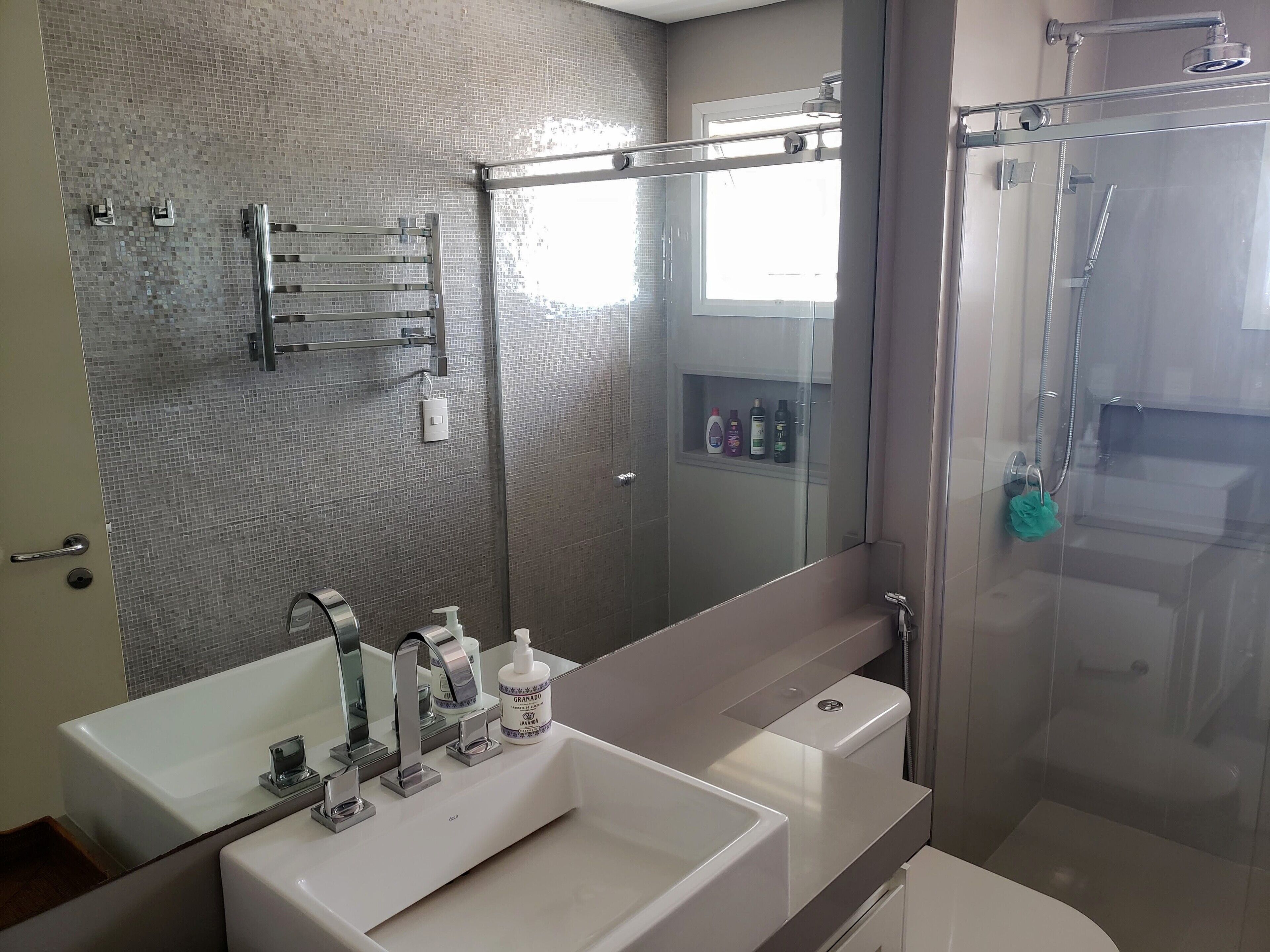 A modern bathroom with a glass shower enclosure, a large mirror, and a vanity with a sink and two bottles of shampoo.