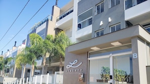 A modern building with a glass entrance, a sign reading "LIBERTY RESIDENCE," and a gated driveway with palm trees. - Cobertura Liberty Campeche (Florianópolis)