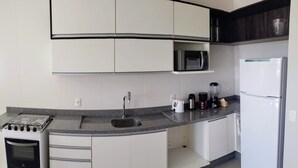 A modern kitchen with white cabinets, a built-in microwave, a gas stove, and a refrigerator. - Cobertura Liberty Campeche (Florianópolis)
