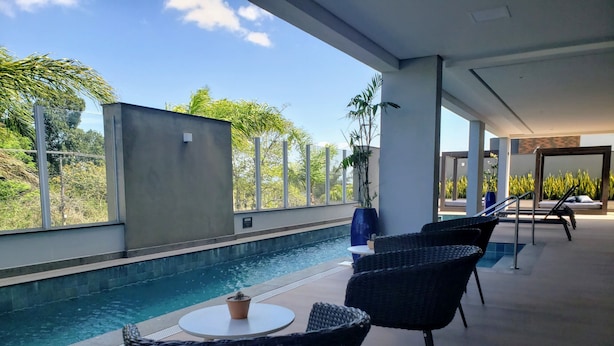 A poolside area with a view of the pool, wicker chairs, a small table, and a potted plant. - Cobertura Liberty Campeche (Florianópolis)