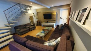 Una sala de estar moderna con una escalera, un conjunto de sofás, una mesa de centro y un televisor de pantalla plana.
