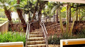 Una escalera de piedra con barandales metálicos, rodeada de abundante vegetación y un muro de piedra.