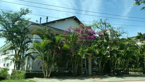 Un edificio residencial con techo de tejas, rodeado de abundante vegetación y plantas con flores.