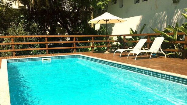 Una piscina rectangular con una terraza de madera y sillas reclinables blancas.