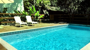 Una piscina rectangular con agua azul cristalina, rodeada por un deck de madera y un borde de azulejos.