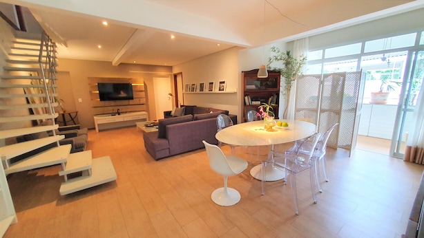 Una sala de estar moderna con un sofá, un televisor, una mesa de comedor con sillas y una escalera.