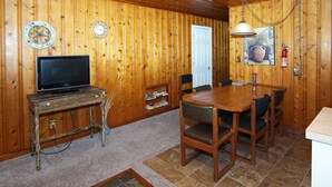 Une pièce aux murs lambrissés, avec une télévision posée sur une table en bois, une porte et un tableau représentant un pot.
