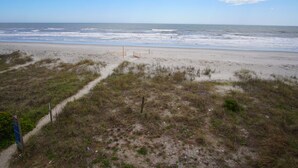 Une plage avec un sentier de sable menant à une clôture en bois, d’où l’on a une vue sur l’océan.