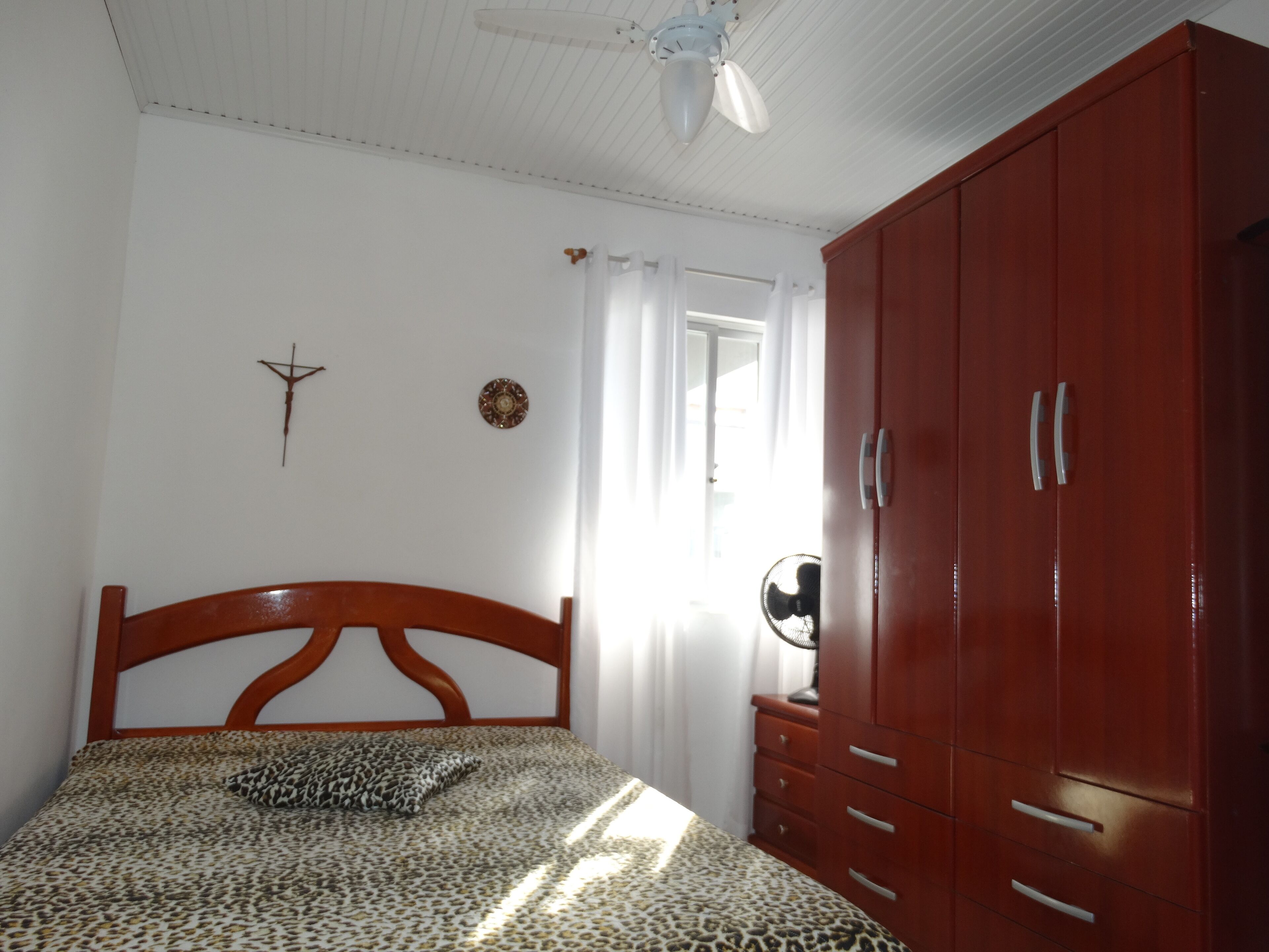 A bedroom with a wooden bed, a wardrobe, a ceiling fan, and a window with curtains.