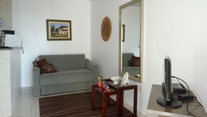 Een woonkamer met een grijze bank, een klein houten tafeltje, een televisie en een grote spiegel aan de muur.