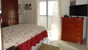 Een slaapkamer met een bed, een dressoir, een televisie en een raam met gordijnen.