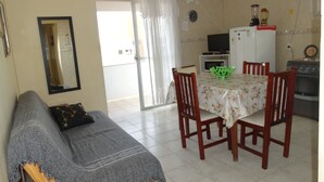 Una sala acogedora con un sofá, una mesa de comedor con sillas, una zona de cocina con electrodomésticos y un ventanal corredizo que da a un espacio exterior.