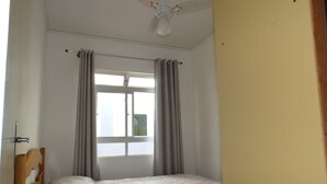 Un dormitorio con dos camas, una ventana con cortinas, un ventilador de techo y un radiador.