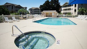 A swimming pool area with a hot tub, lounge chairs, and a fenced pool deck.
