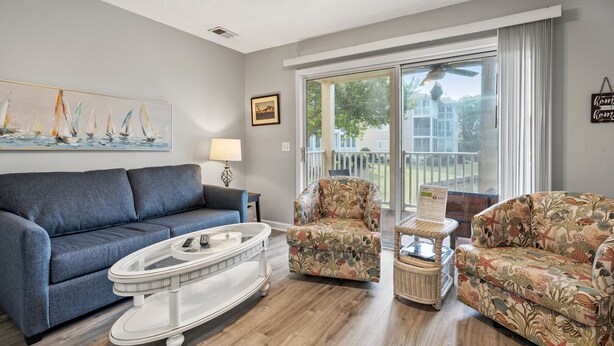 A living room with a blue sofa, two floral armchairs, a white coffee table, and a painting of sailboats.