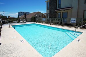 Una piscina rectangular con zona poco profunda, rodeada por una valla de madera y un letrero de salvavidas.