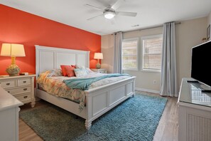 Un dormitorio con cama, mesitas de noche, televisor y ventilador de techo.