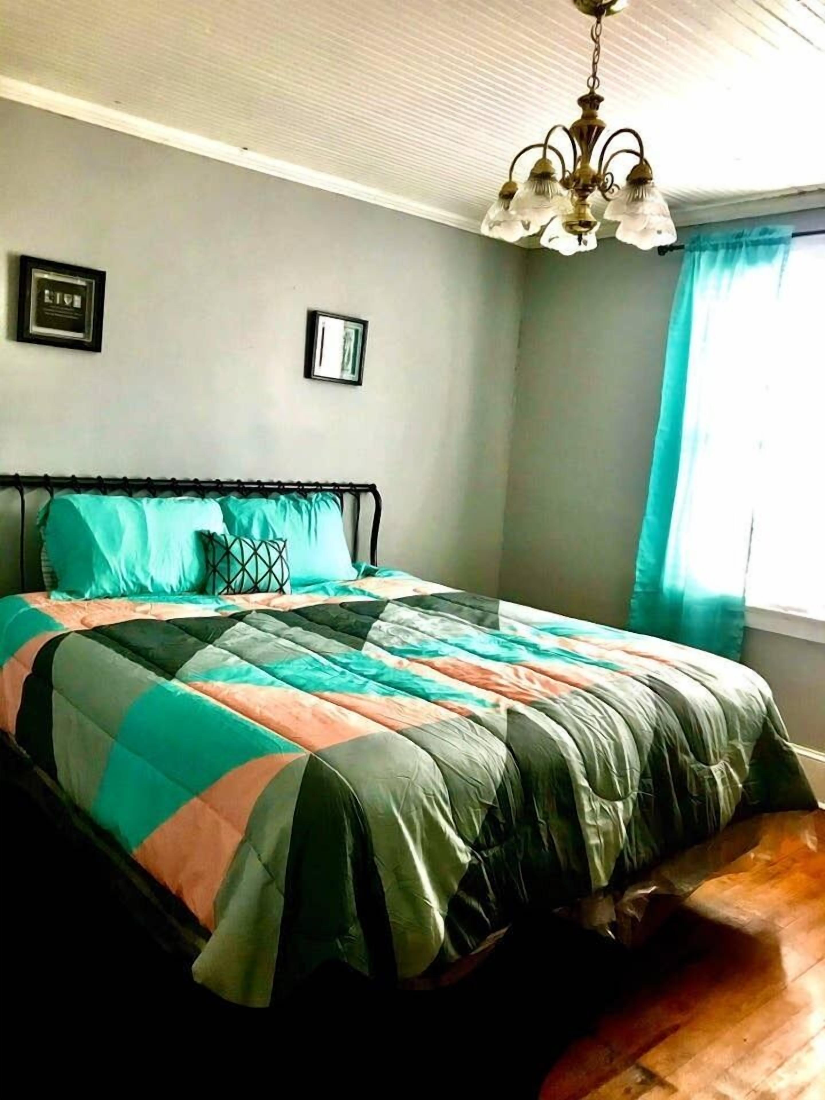A bedroom with a bed, a chandelier, and a window with curtains.