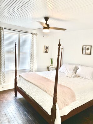 A neatly made bed with a wooden frame, a ceiling fan, and a window with blinds. - Bella's Boutique Hotel (Hemingway)