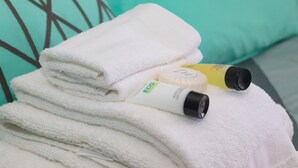 A stack of white towels with a bottle of lotion and a yellow bottle on top. - Bella's Boutique Hotel (Hemingway)