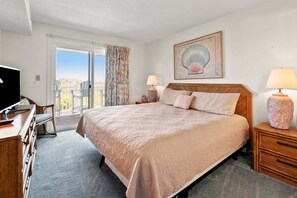 A hotel room with a large bed, a television, a desk, and a balcony with a view. - Cozy corner condo w/amazing ocean views, private porch, pool and non-stop sunrises/sunsets (North Myrtle Beach)
