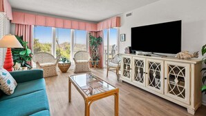 Un salon comprenant un canapé, des fauteuils, un téléviseur, une table basse en verre et un meuble.