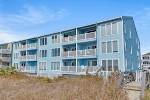 A multi-story building with balconies, a wooden deck, and a clear sky. - Cozy corner condo w/amazing ocean views, private porch, pool and non-stop sunrises/sunsets (North Myrtle Beach)