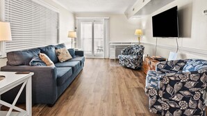 A modern living room with a sofa, armchair, and a flat-screen TV. - Soothing stay at this oceanfront condo w/pool, sundeck, priv balc, grill in popular North Myrtle (North Myrtle Beach)
