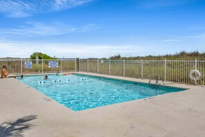 A rectangular pool with a metal fence, shallow water warning signs, and a lifeguard chair.