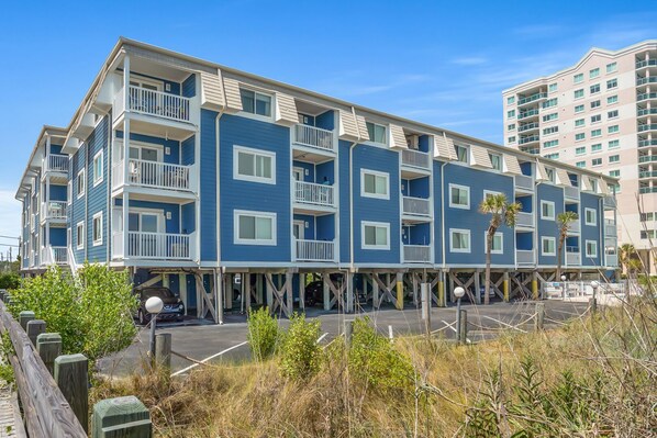 A multi-story hotel with balconies, a parking area, and a beach view.