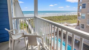 A balcony with white plastic chairs, a pool, and a view of the beach and ocean. - Soothing stay at this oceanfront condo w/pool, sundeck, priv balc, grill in popular North Myrtle (North Myrtle Beach)
