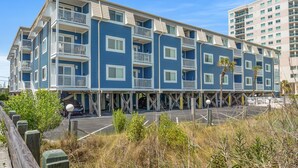 Un hotel de varios pisos con balcones, zona de estacionamiento y vista al mar.