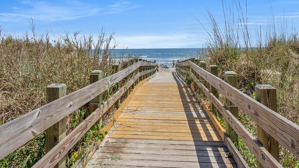 Un paseo marítimo de madera que lleva a una playa con cielo despejado.