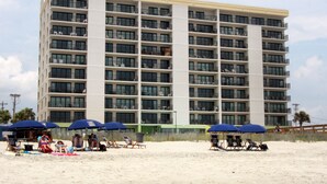 A multi-story hotel with balconies, beach chairs, and umbrellas on the sand in front. - Panoramic ocean views, pool, hot tub, close to shops, restaurants and Cherry Grove Beach (North Myrtle Beach)