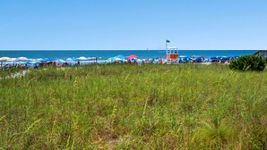 A beach with a lifeguard tower, umbrellas, and people. - Panoramic ocean views, pool, hot tub, close to shops, restaurants and Cherry Grove Beach (North Myrtle Beach)