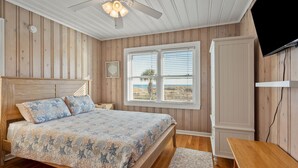 A bedroom with a wooden bed, a nightstand, a desk, a TV, and a window with a view. - Oceanfront, dog-friendly vacation home w/gorgeous ocean views, large deck-steps from beach (North Myrtle Beach)