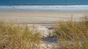 A beach with sand and grass in the foreground, and the ocean in the background. - Oceanfront, dog-friendly vacation home w/gorgeous ocean views, large deck-steps from beach (North Myrtle Beach)