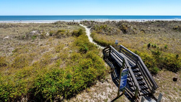 A wooden boardwalk leading to a beach with a clear view of the ocean.