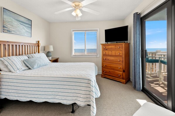 A bedroom with a bed, a dresser, a ceiling fan, a TV, and a window with blinds.