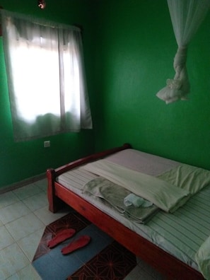 A room with a single bed, green walls, a window with white curtains, and a mosquito net hanging above the bed. - Prudence Guest House (Bondo)