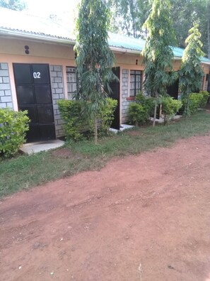 A building with numbered doors, a dirt path, and surrounding greenery. - Prudence Guest House (Bondo)