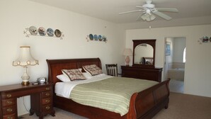 A bedroom with a wooden bed, a nightstand, a dresser, a ceiling fan, and a mirror. - Rehoboth Beach Condo (Rehoboth Beach)