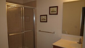 A bathroom with a glass shower enclosure, a sink with a mirror, and a towel rack. - Rehoboth Beach Condo (Rehoboth Beach)