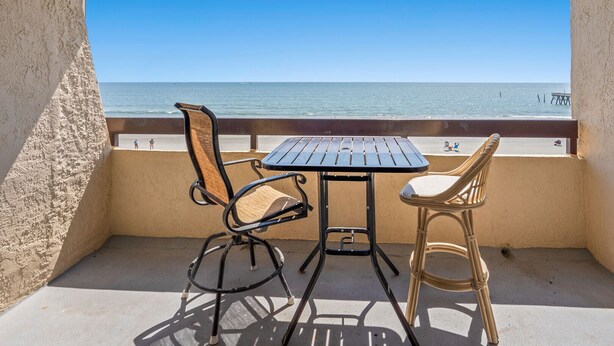 A balcony with a table and two chairs, overlooking a beach and the sea. - Rest, pure & simple! Gorgeous ocean view, large balcony w/pool & hot tub in popular Cherry Grove (North Myrtle Beach)