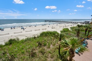 A beach with a wooden pier extending into the ocean, sandy beach, and some greenery in the foreground.