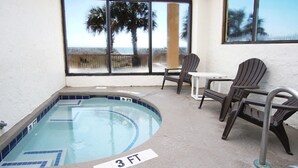A small indoor pool with a 3 FT depth marker, surrounded by patio chairs and a table, with a view of palm trees and the beach through large windows. - Rest, pure & simple! Gorgeous ocean view, large balcony w/pool & hot tub in popular Cherry Grove (North Myrtle Beach)